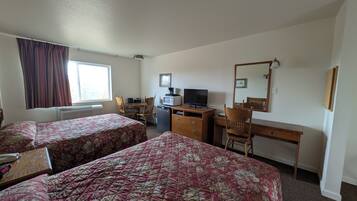 A hotel room with two beds, a desk, a chair, a television, a microwave, and a window with curtains.