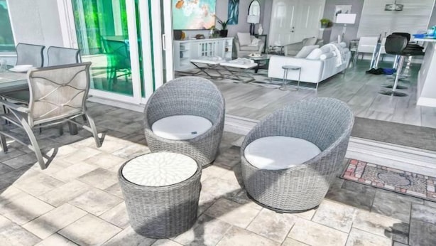 A modern living room with wicker furniture, a glass door leading outside, and a white sofa set. - Phoenix, quite Area, Pool and great water few (Cape Coral)