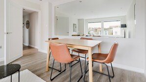 Ein moderner Essbereich mit einem Holztisch, Ledersesseln, einem großen Spiegel und Blick auf die Stadt durch ein Fenster.