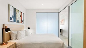 Ein modernes Schlafzimmer mit einem großen Bett, einem Nachttisch mit Lampe, einem Kleiderschrank und einer Glaswand.