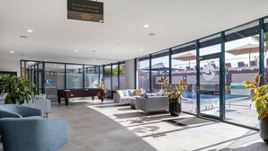 Un vestíbulo moderno con mesa de billar, asientos cómodos y ventanas amplias que ofrecen vistas al área de la piscina.