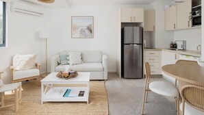 Una cocina moderna con un refrigerador de acero inoxidable, un comedor con una mesa y sillas de madera, y una sala de estar con un sofá y una mesa de centro.