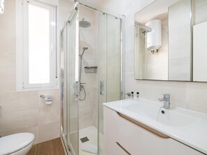 Een moderne badkamer met een douchecabine van glas, een witte wastafel en een spiegel boven de wastafel.