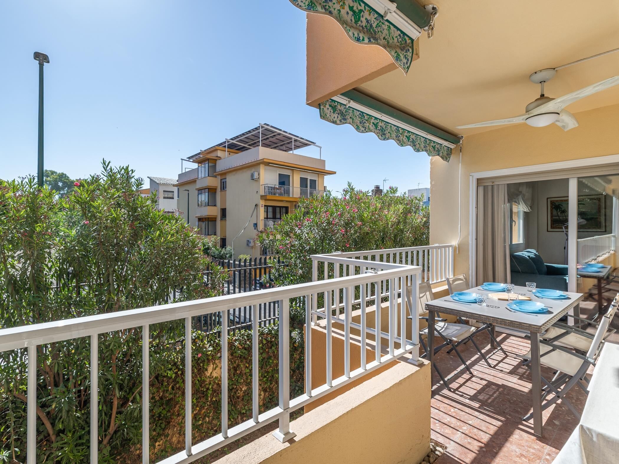 Un balcon extérieur avec une table dressée pour les repas, un ventilateur de plafond et une vue sur les bâtiments voisins.