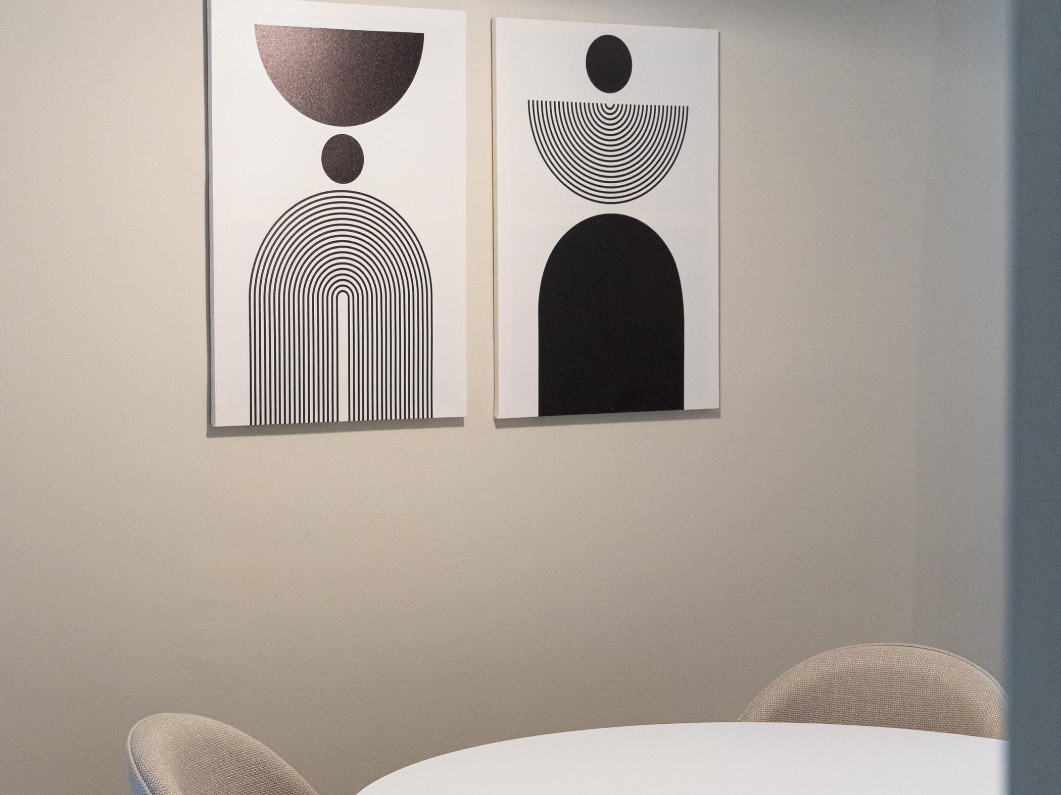 Zwei abstrakte Kunstwerke an einer Wand in einem Raum mit einem runden Tisch und Stühlen.
