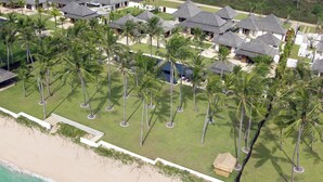 Vista aérea de un resort con varias cabañas, un césped cuidado y acceso a la playa.