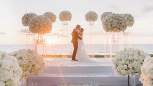 Una ceremonia de boda con una pareja besándose bajo un arco floral frente al mar.