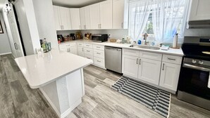 Een moderne keuken met witte kasten, een centraal eiland, roestvrijstalen apparatuur en een raam met lichte gordijnen.