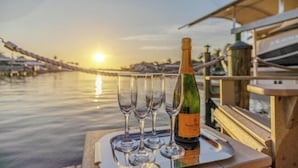 Eine Flasche Veuve Clicquot Champagner auf einem Tablett mit vier Gläsern, vor einer Sonnenuntergangsansicht von einem Boot aus.