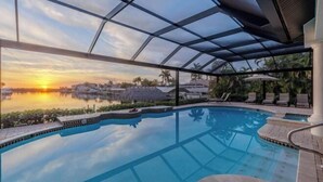 Ein Swimmingpool mit Glasdach, umgeben von Liegestühlen und Palmen, mit Blick auf den Sonnenuntergang.