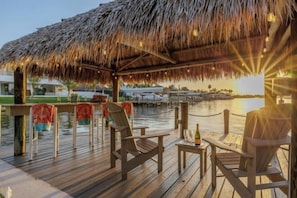 A wooden deck with chairs and a table, a thatched roof, and a view of the water. - Villa Terracotta (Cape Coral)