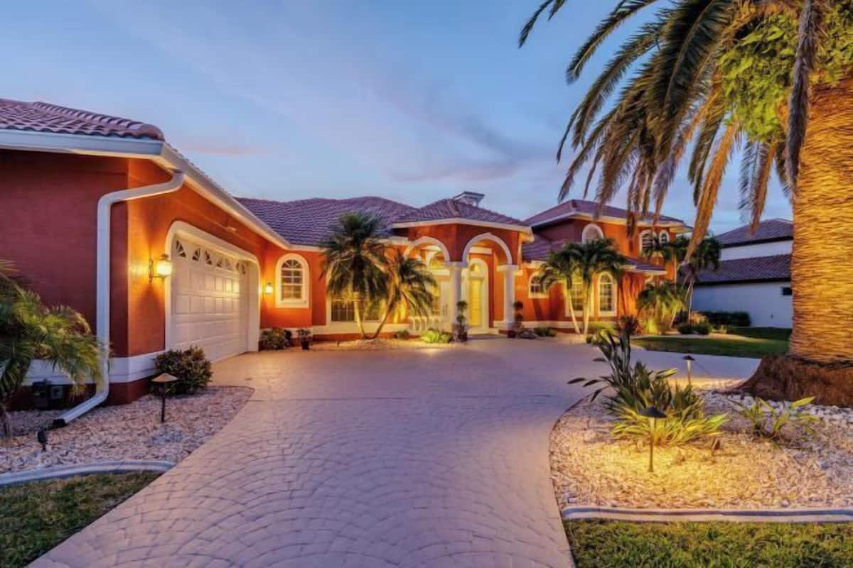 A residential property with a paved driveway, a garage, and a well-maintained lawn with palm trees.