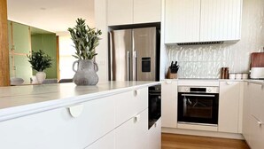 Une cuisine moderne avec des meubles blancs, un réfrigérateur en acier inoxydable, un four encastré et un plancher en bois.