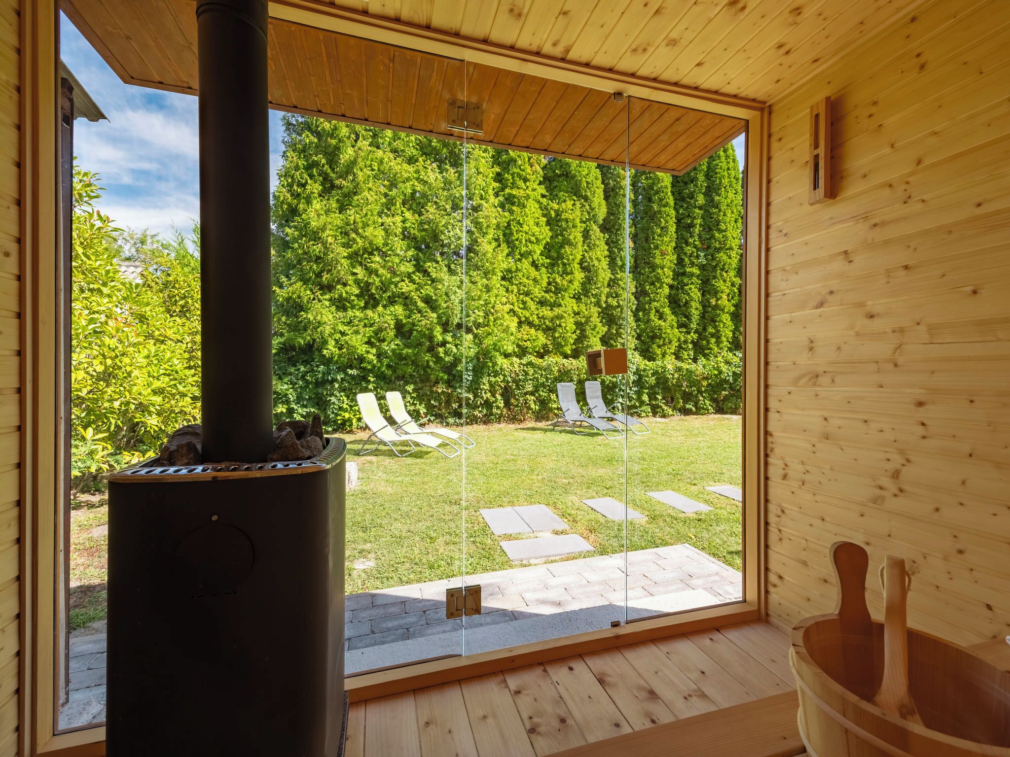 A wooden cabin with a large glass door leading to a backyard with a barbecue grill, outdoor seating, and a wooden hot tub.