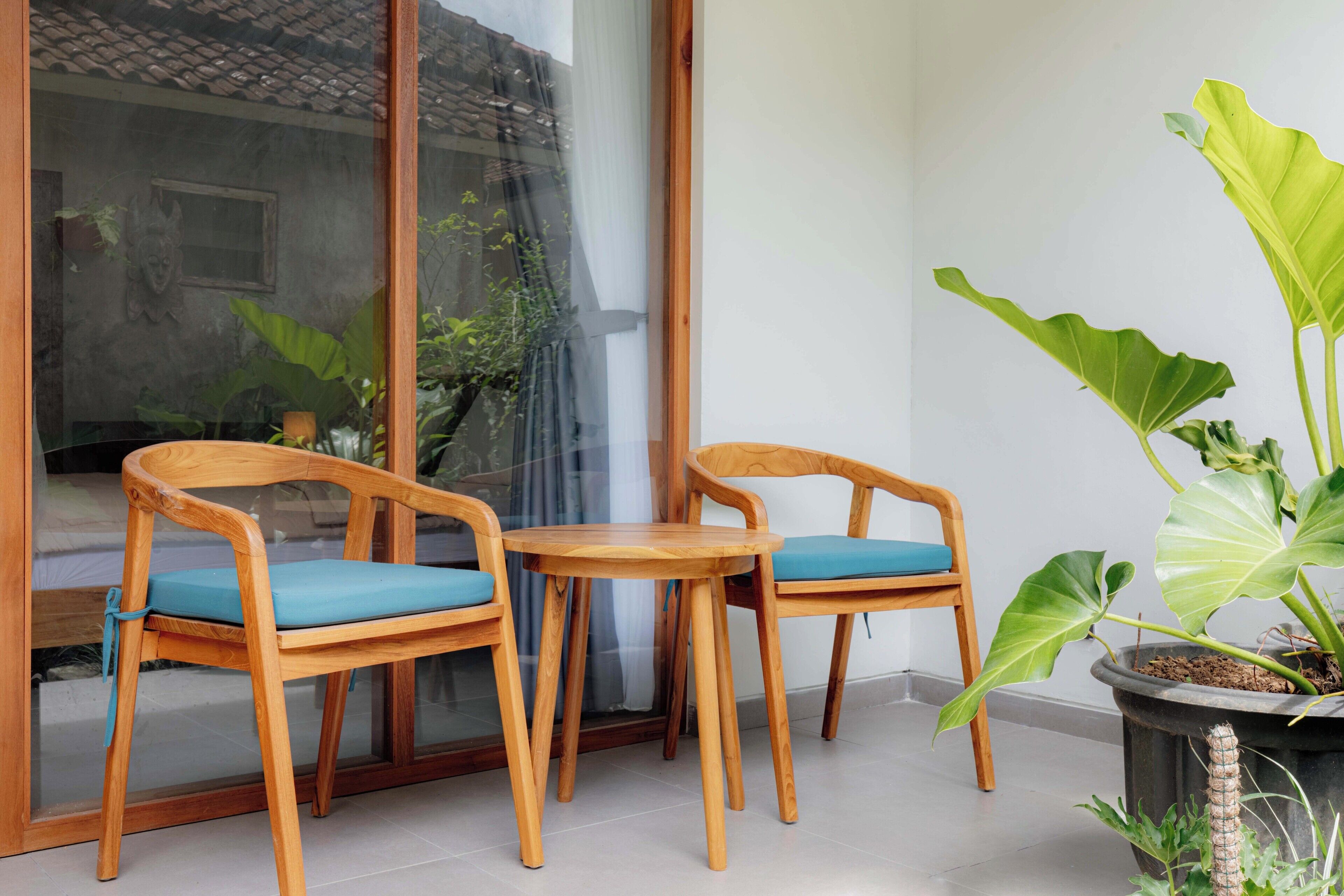 Two wooden chairs with blue cushions and a small round table in a room with a large window and a potted plant.
