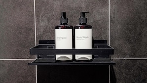 Due flaconi di shampoo e bagnoschiuma su un ripiano nero, con uno sfondo a parete piastrellata.