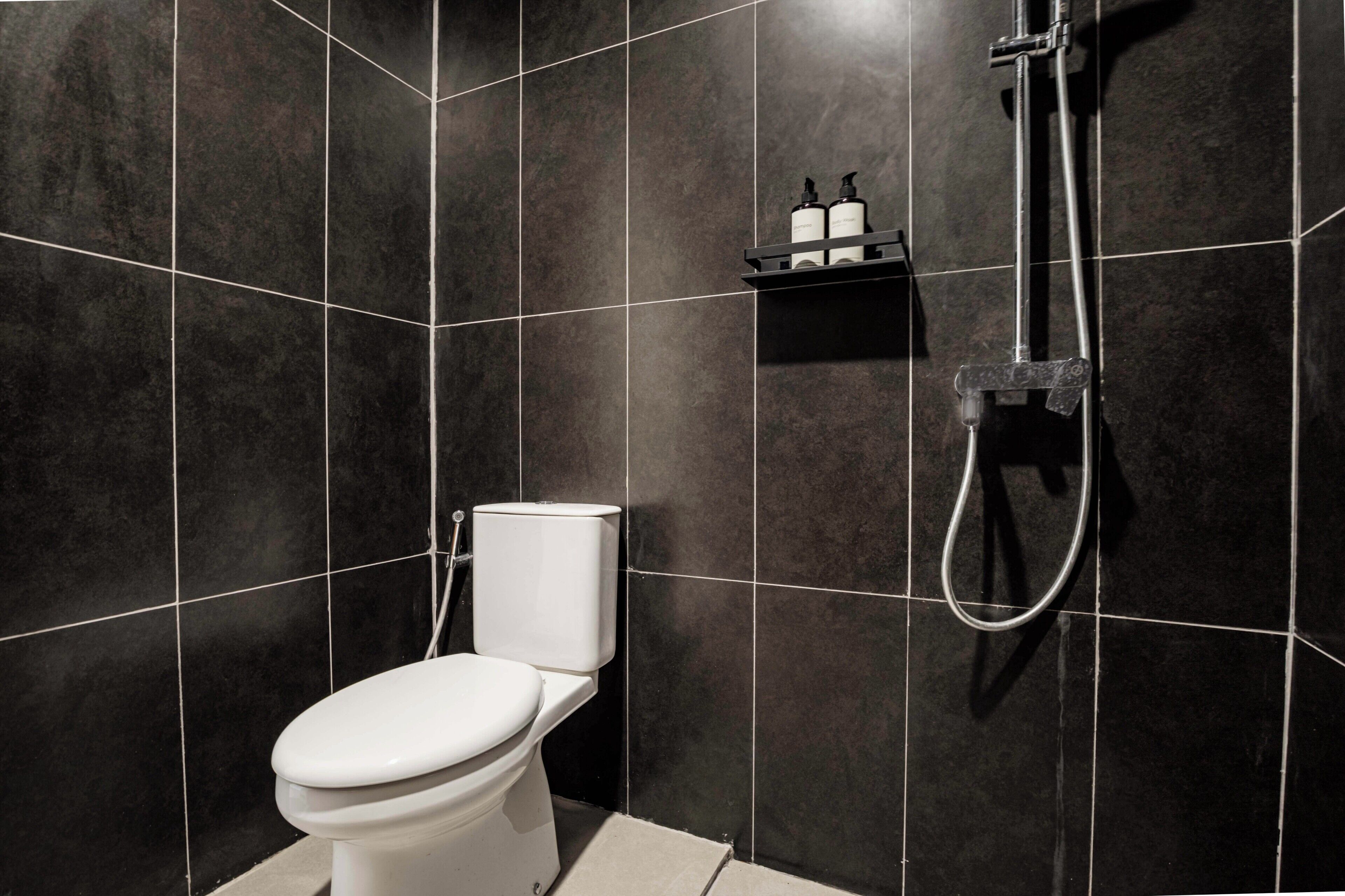 Une salle de bain moderne avec des carreaux de couleur sombre, des toilettes, une douche et une étagère contenant des articles de toilette.
