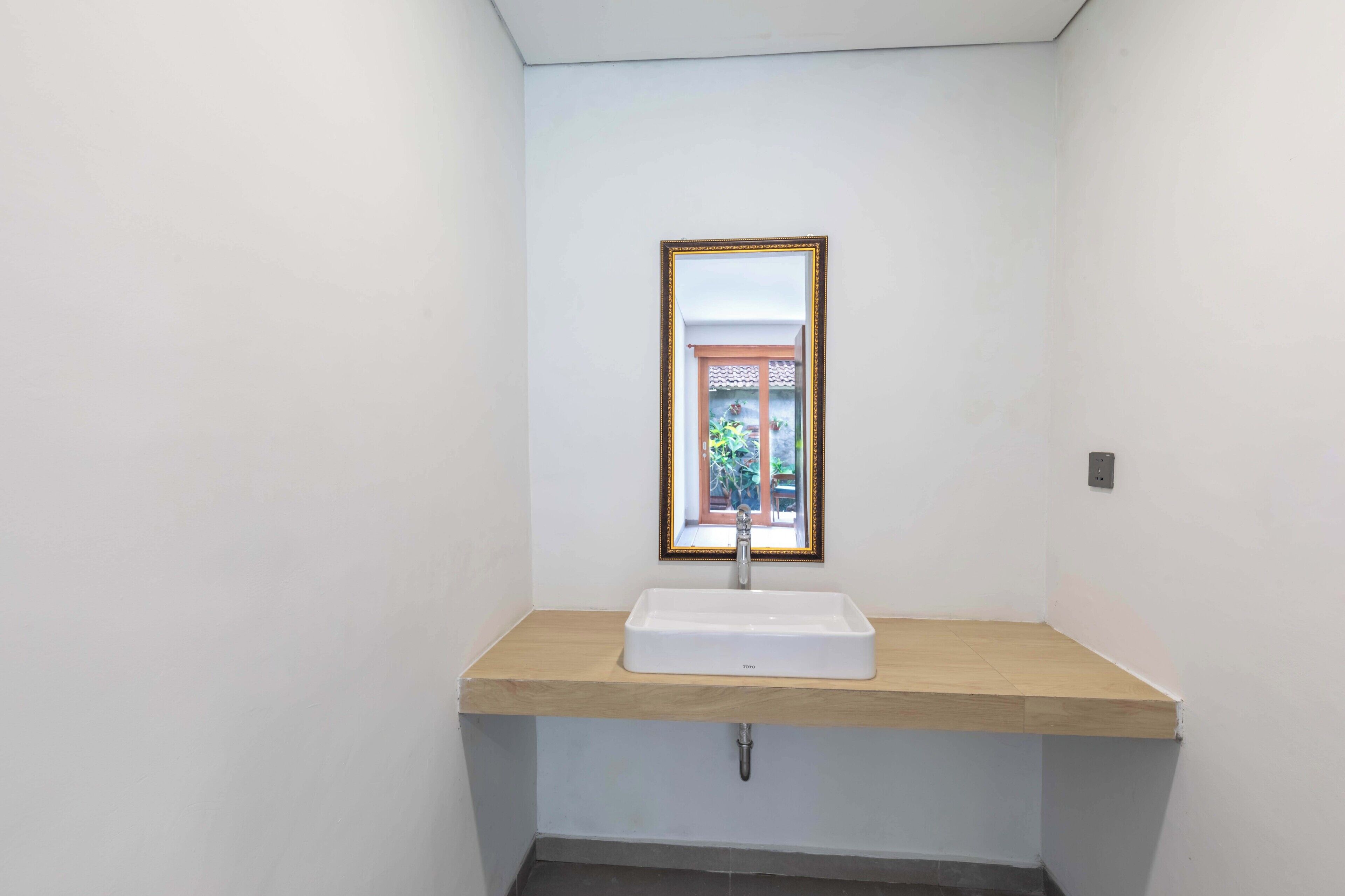 A bathroom with a white sink, wooden countertop, and a mirror with a decorative frame.