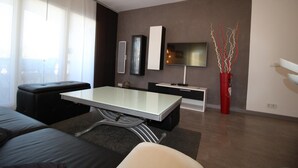 A modern living room with a glass-top dining table, black sofas, a flat-screen TV, and a red vase with branches. - CALA FONDA Apartment in Santa Margarita Roses (ROSES)