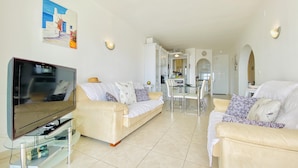 A modern living room with a flat-screen TV, two sofas, a glass coffee table, and a dining area with a glass table and chairs. - CENTRAL Apartment Roses near the beach with sea view (Roses)