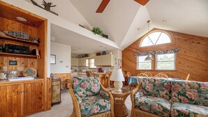 Ein gemütliches Interieur mit Holzwänden, einem Essbereich mit Korbmöbeln und einer Küche im Hintergrund.