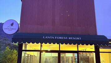 A resort entrance with a large glass door, outdoor seating area, and a sign reading "LANTA FOREST RESORT".