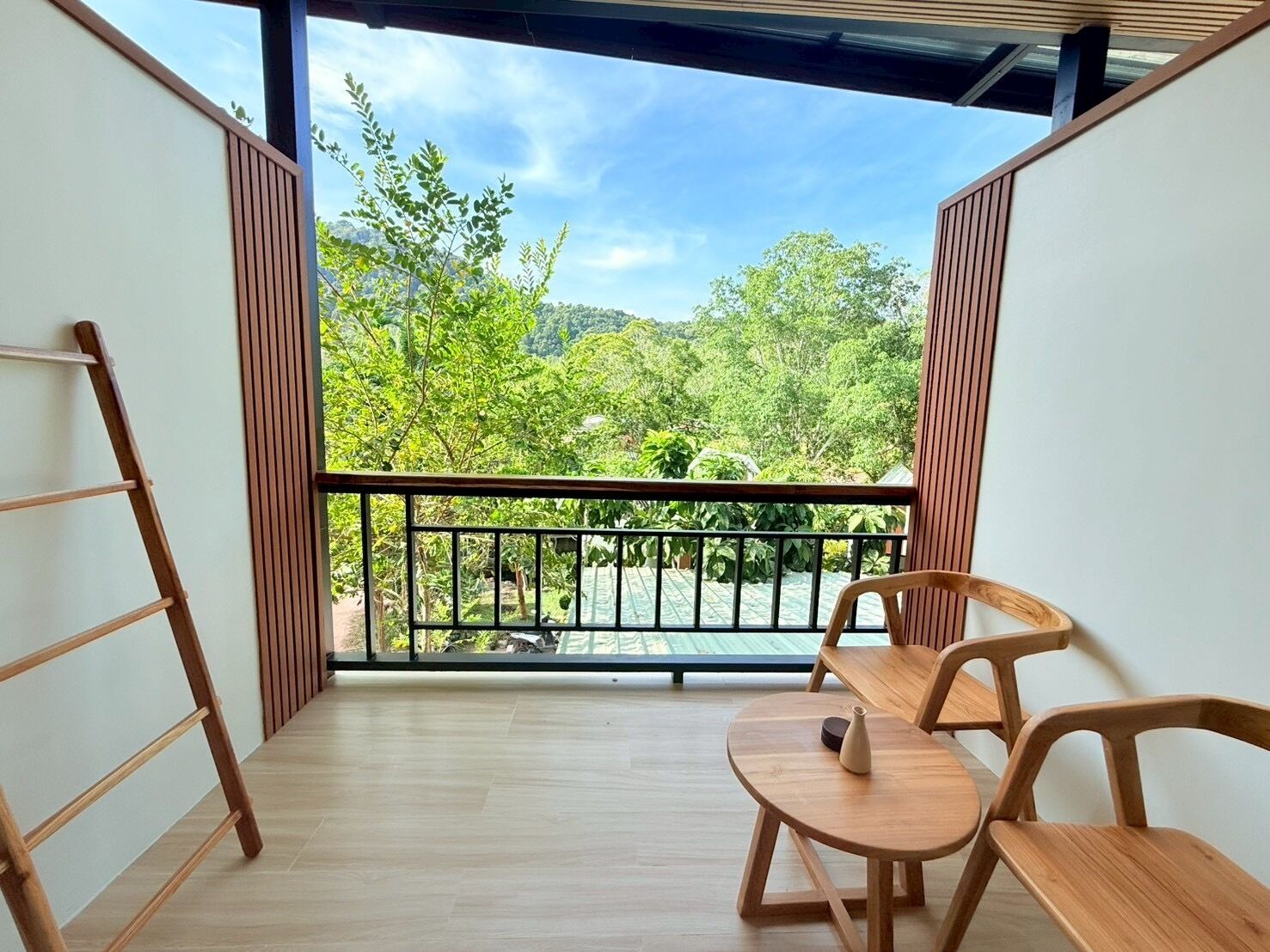 A balcony with a wooden floor, a black railing, and a view of lush greenery.