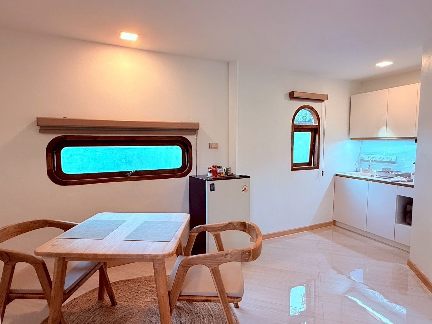 Une cuisine compacte avec une fenêtre, un coin repas comprenant une table et des chaises, et un petit réfrigérateur.