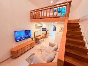 A modern living room with a wooden staircase, a TV mounted on the wall, and a cozy seating area. - Lanta Forest Resort&Villas  (Ko Lanta)