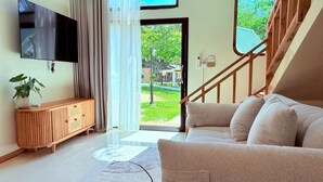 A modern living room with a sofa, a wooden cabinet, a TV, and a staircase leading to an outdoor area. - Lanta Forest Resort&Villas  (Ko Lanta)
