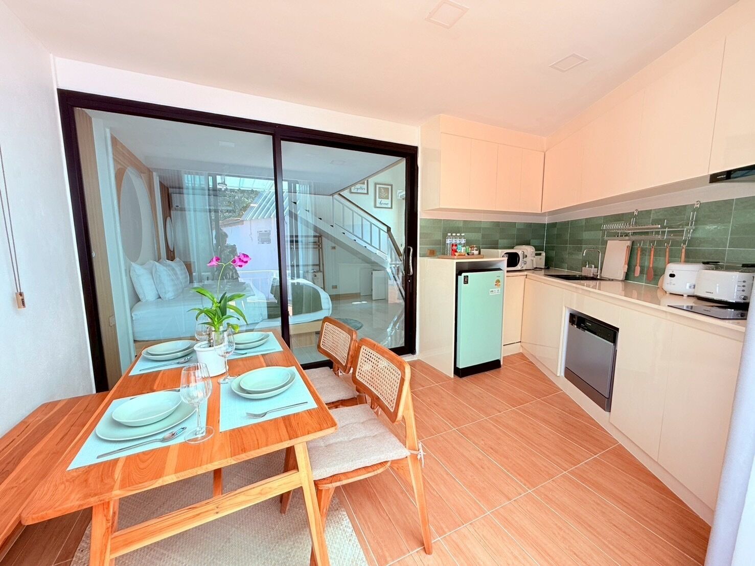 A modern kitchen with a dining area, featuring a wooden table set for two, a small fridge, and a dishwasher.