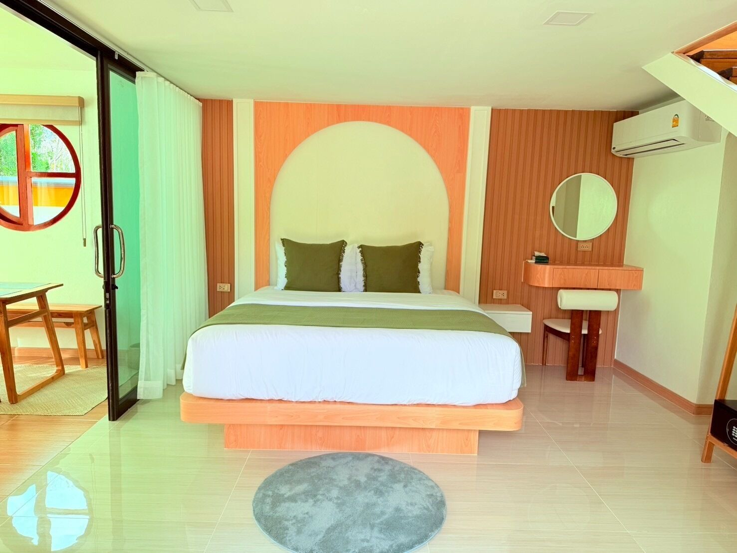 A bedroom with a large bed, a bedside table, a mirror, and an air conditioning unit.