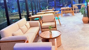 A modern indoor seating area with sofas, tables, and chairs, large windows offering views of greenery outside. - Lanta Forest Resort&Villas  (Ko Lanta)