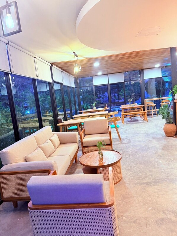 A modern indoor seating area with sofas, tables, and chairs, large windows offering views of greenery outside. - Lanta Forest Resort&Villas  (Ko Lanta)