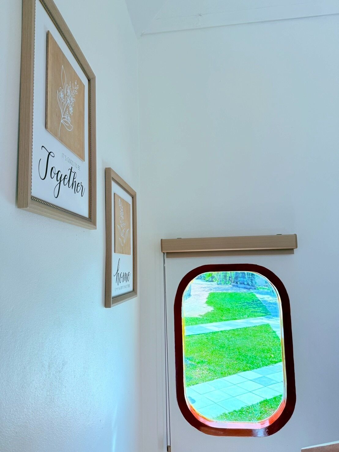 A room with a window, framed artwork, and a wooden shelf.