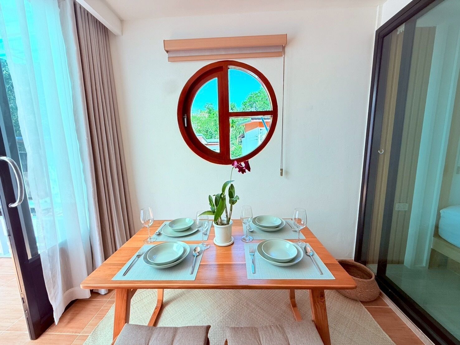A dining area with a table set for four, a potted plant, and a window with a view of greenery.