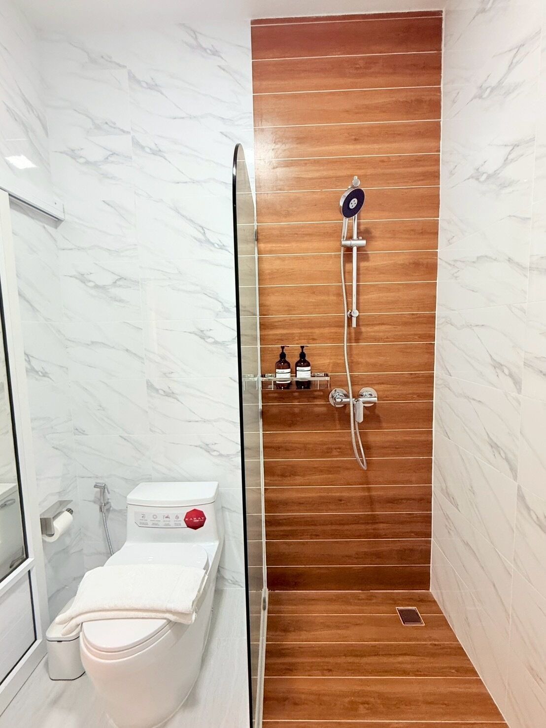 Une salle de bain moderne avec une douche à parois de verre, des toilettes blanches et un mur de douche recouvert de panneaux en bois.