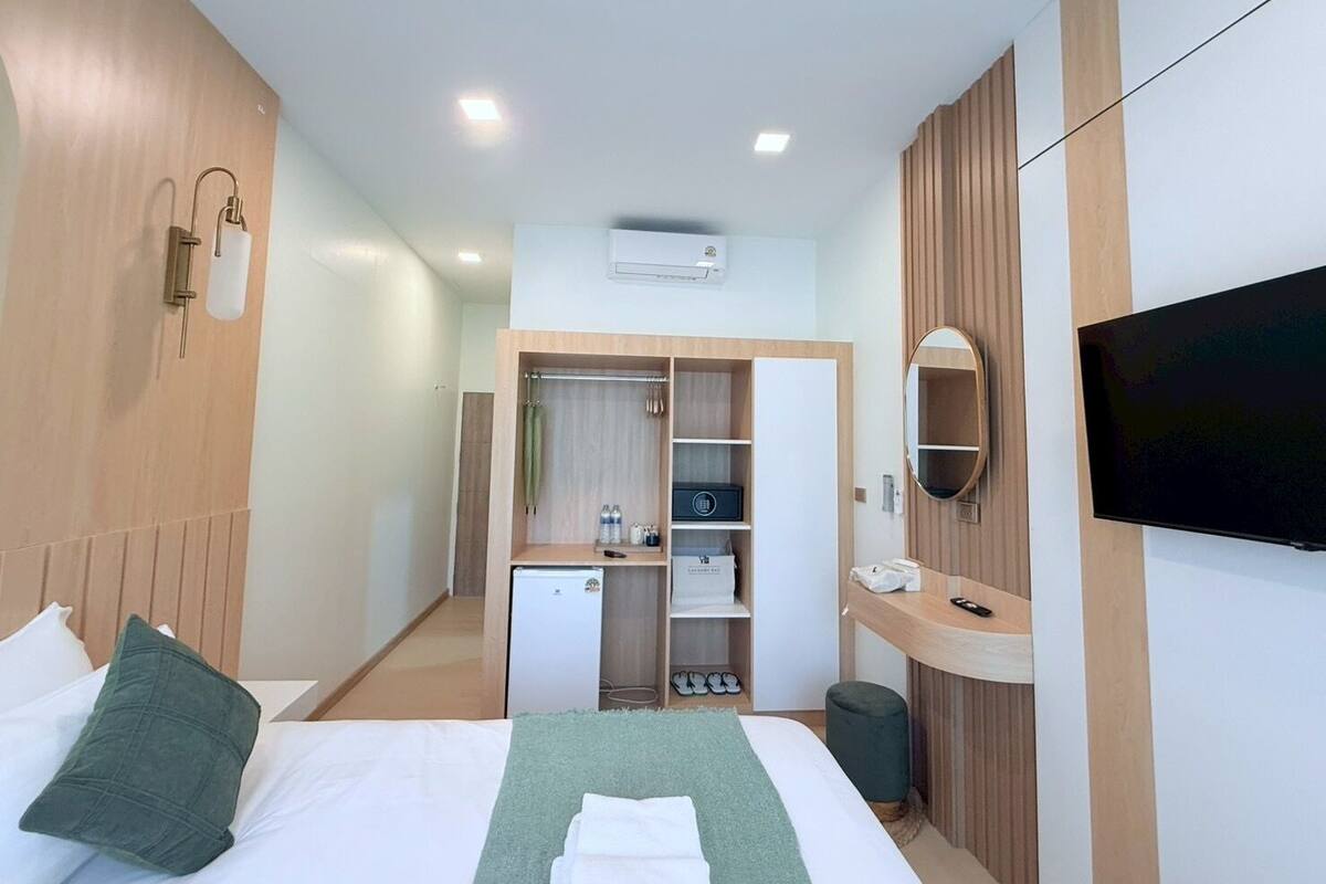A hotel room with a bed, a wardrobe, a small desk with a mirror, a TV, and a mini-fridge.
