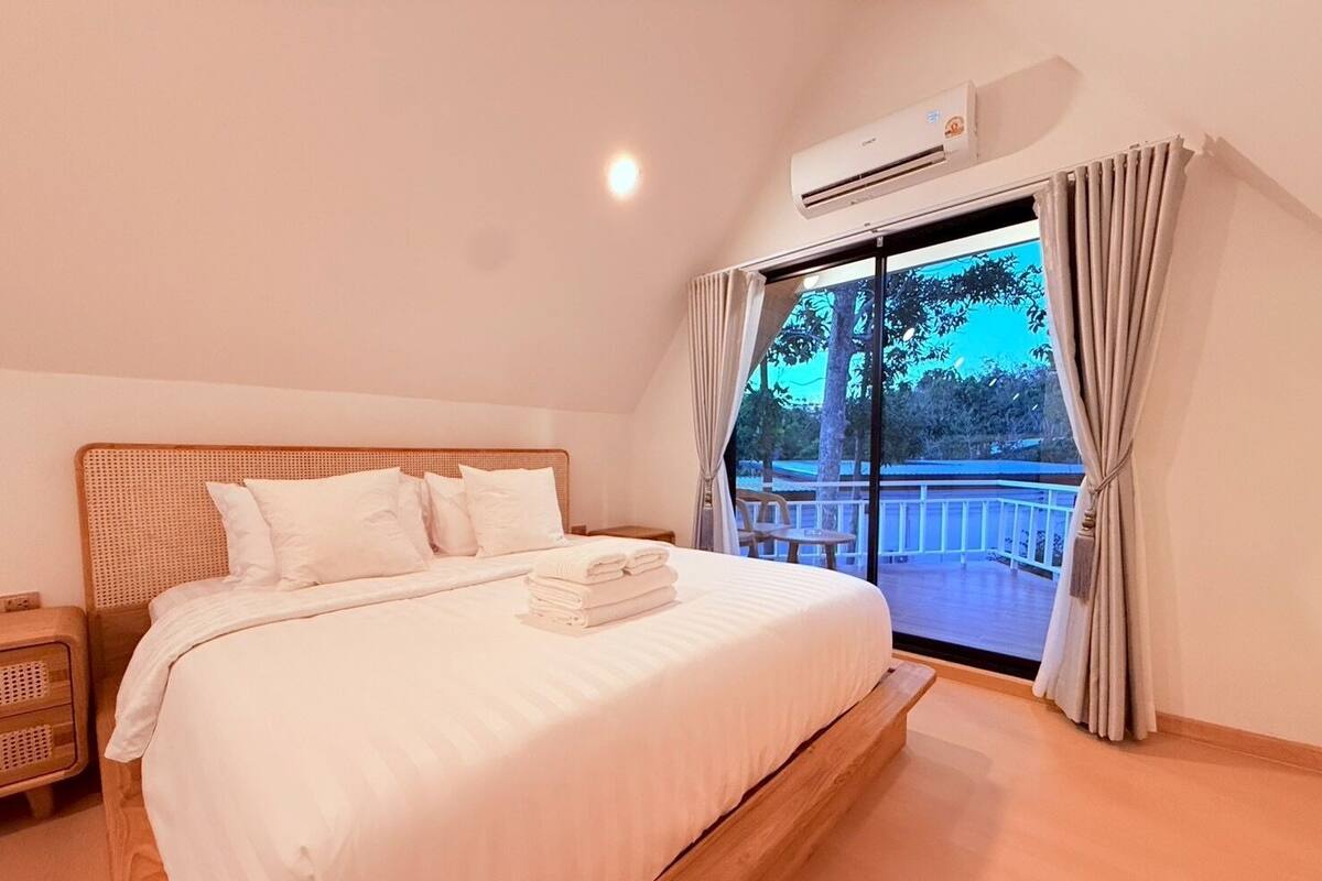 A bedroom with a bed, a nightstand, an air conditioning unit, and a view of an outdoor balcony.