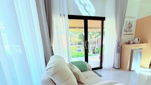 A modern hotel room with a sofa, a small kitchenette, and a sliding glass door leading to a garden. - Lanta Forest Resort&Villas  (Ko Lanta)