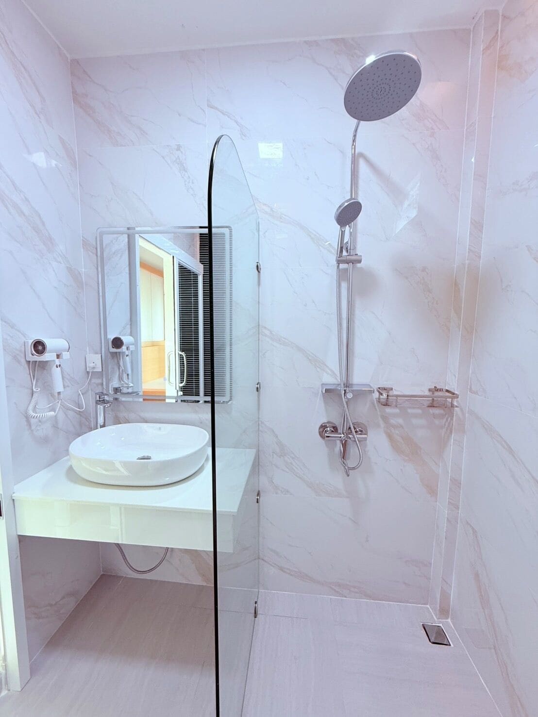 Un baño moderno con lavamanos de mármol blanco, ducha con cerramiento de vidrio y unidad de aire acondicionado a la vista.