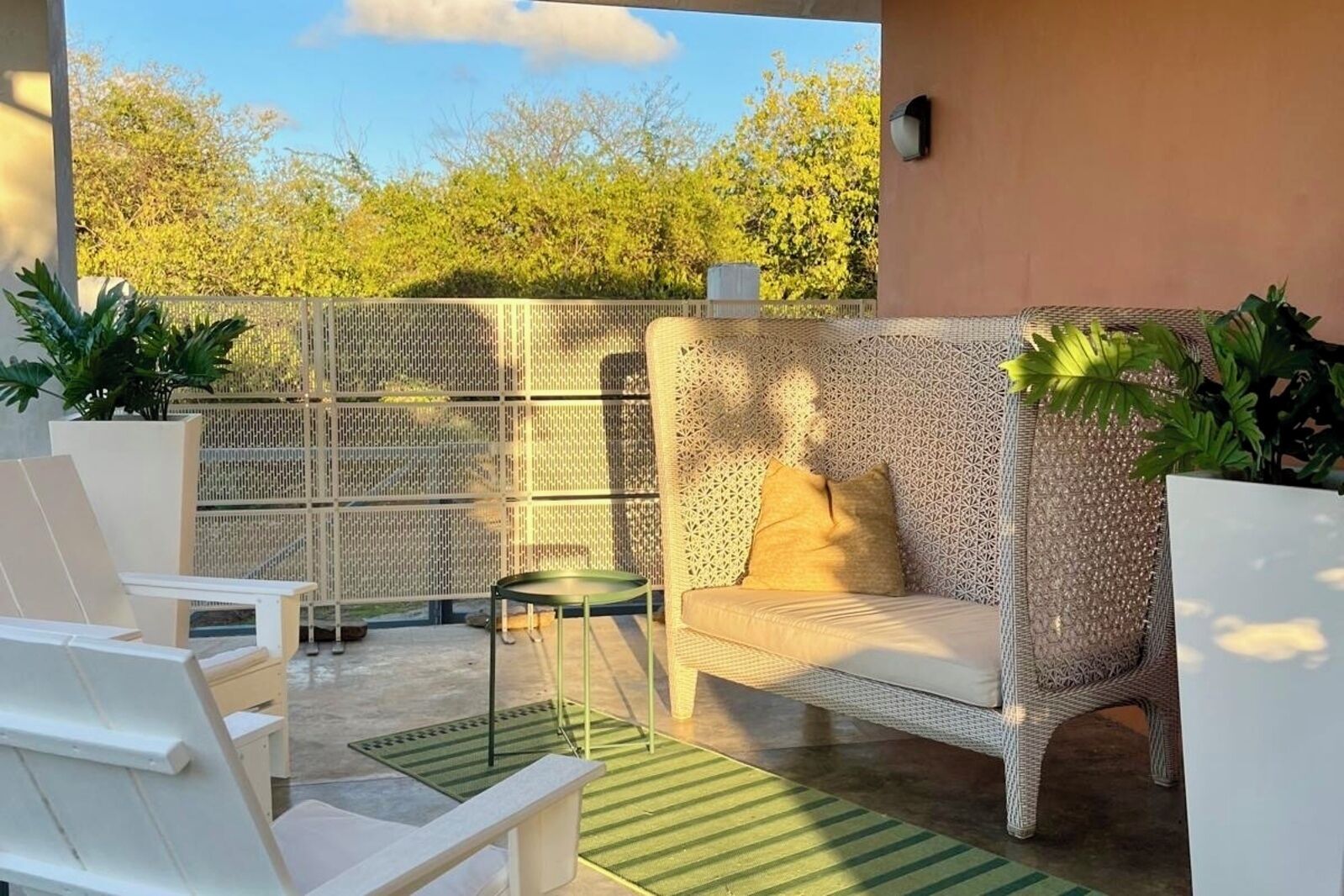 Un patio al aire libre con mobiliario de mimbre blanco, un tapete verde y un muro decorativo.
