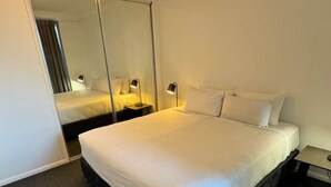 A hotel room with a large bed, a bedside table with a lamp, and a mirror on the wall. - Dreamy Cityside 2BR Haven Brisbane Central (Brisbane City)