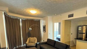 A living room with a sofa, armchair, and a ceiling light. There is a door leading to a bedroom and a kitchen area with a refrigerator. - Dreamy Cityside 2BR Haven Brisbane Central (Brisbane City)