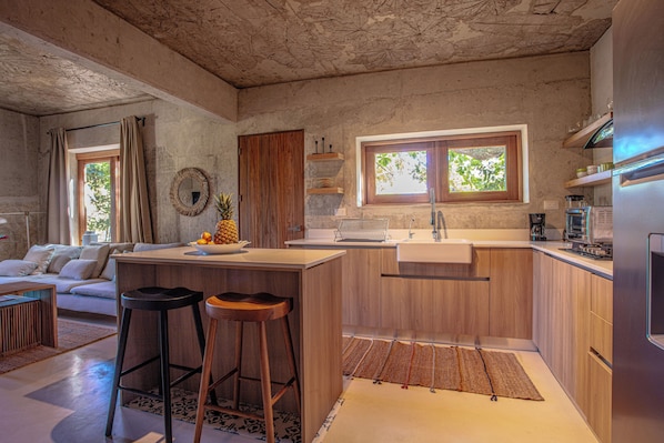 Eine moderne Küche mit Holzausbau, einer zentralen Kochinsel mit Hockern, einem Spülbecken und einem Fenster mit Blick auf Grünflächen.