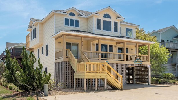 A two-story house with a covered porch and a wooden staircase leading to the entrance. - Seventh Heaven - Corolla, Ocean Sands, 500 Yds to Beach, Pool, Hot Tub, Pool Table, Pets OK (Corolla)