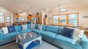 A spacious living room with a sectional sofa, a dining area with wooden chairs, a kitchen with wooden cabinets, and a ceiling fan. - Seventh Heaven - Corolla, Ocean Sands, 500 Yds to Beach, Pool, Hot Tub, Pool Table, Pets OK (Corolla)