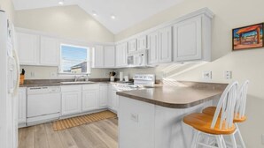 Cucina con mobili bianchi, forno a microonde, piano cottura e isola in legno con due sgabelli da bar bianchi.
