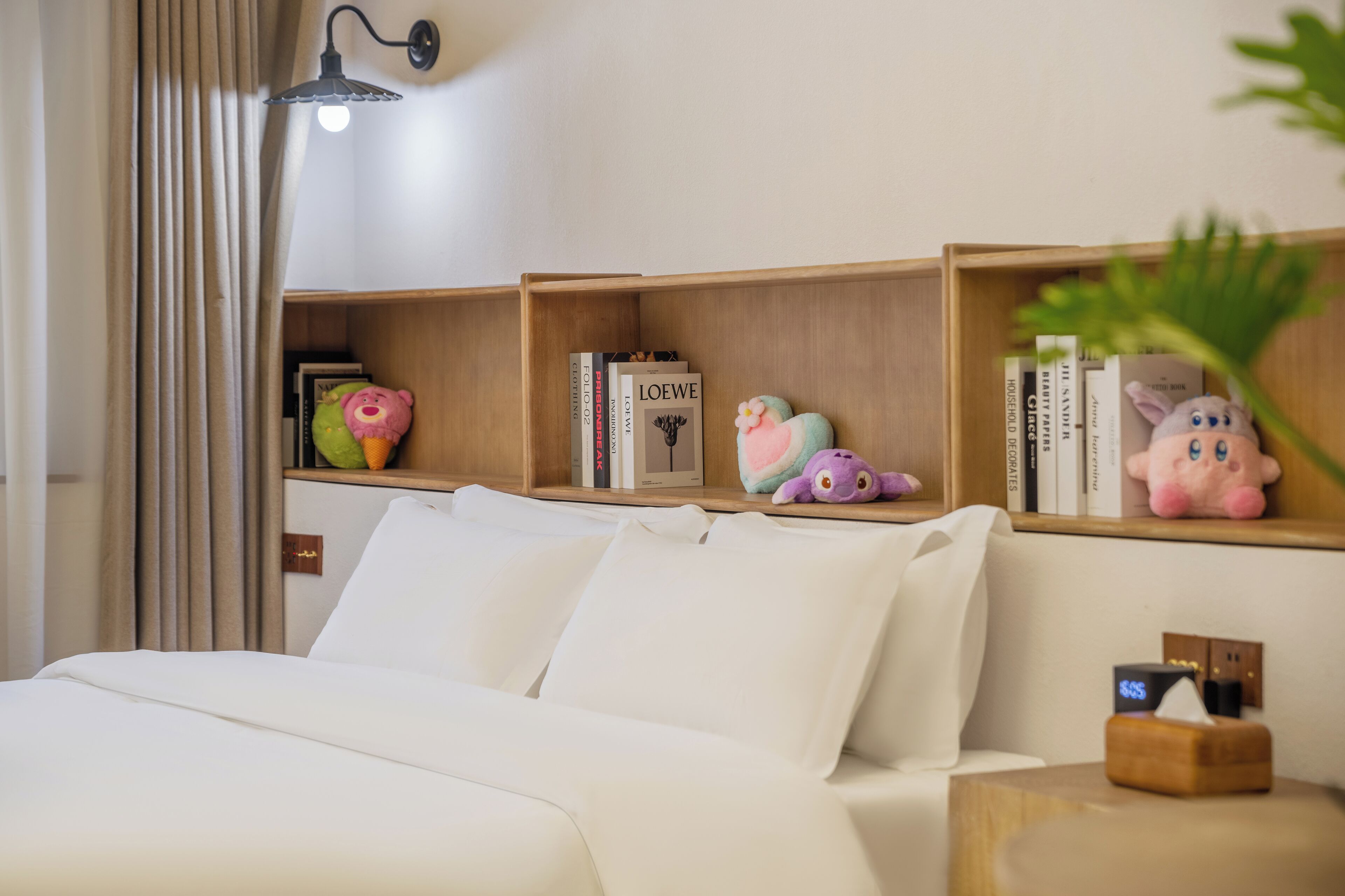 A neatly arranged bedroom with a bed, bedside tables, and shelves with books and plush toys.