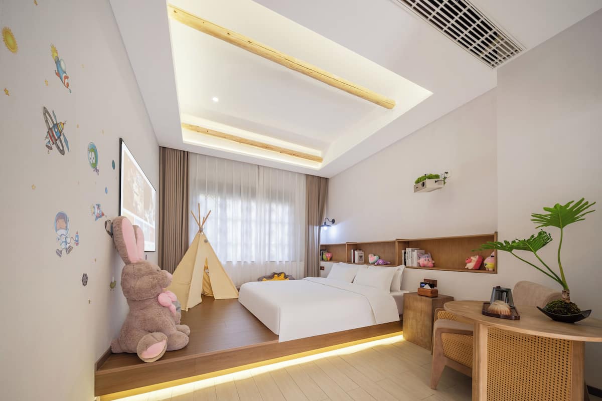 A modern hotel room with a bed, a seating area, a small table, and a window with curtains.